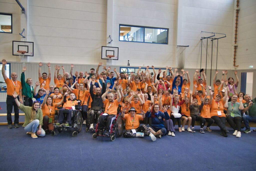 Viele Menschen mit und ohne Handicap in einer Turnhalle bei der Veranstaltung ‚Spitzensport trifft Handicap 2024‘ – Sportlerinnen, Sportler und Teilnehmende begegnen sich in einem inklusiven Umfeld.